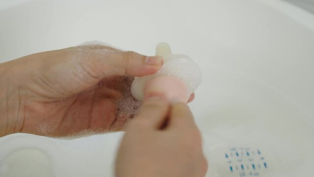 mother hand washing the baby plastic nipple of milk bottle