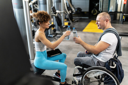 A physically challenged person without obstacles workout at the gym with his female fitness instructor. They're taking a break to refresh and eat energy bars.