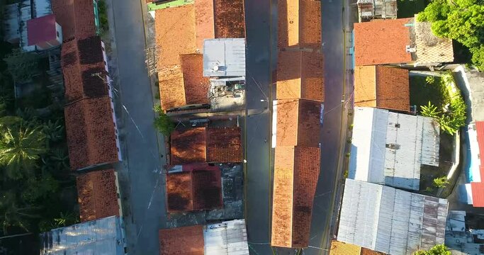 Aerial shot top down small tropical village with red roofs houses,  tilt up reveal green mountanis