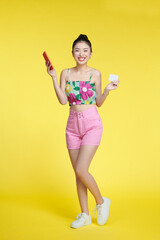 Portrait of a smiling woman holding credit card and mobile phone over yellow background