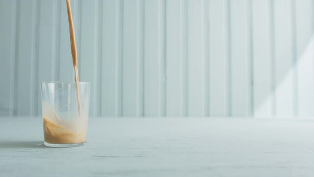 Cafe latte being poured into glass on countertop. Slow motion with copy space