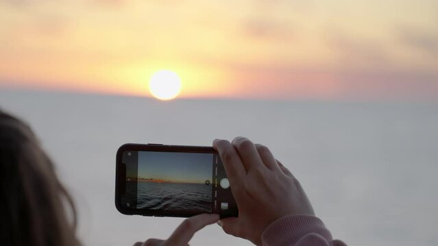 Woman taking a picture of sunset on mobile phone