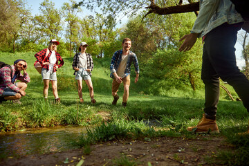 Having fun. Group of friends, active young people going hiking, walking in forest, jumping over river on warm spring day. Concept of active lifestyle, nature, sport and hobby, friendship