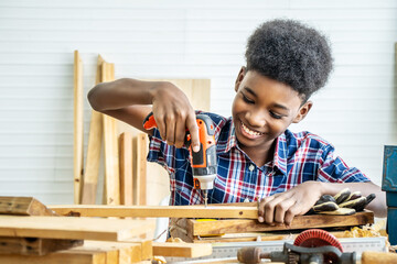 Portrait of african american little child wearing shirt with a drill in hands and help dad assembling furniture shelf with power screwdriver tool, learning concept.