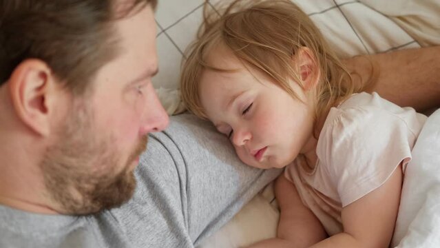 Father and his little daughter toddler girl sleeping together. Healthy sleep. Happy Loving family parent and child sleeping white bed at home. Authentic lifestyle fatherhood moments. Single dad life.