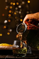 Vertical shot of a hand pouring whisky into a glass with bokeh lights in the background
