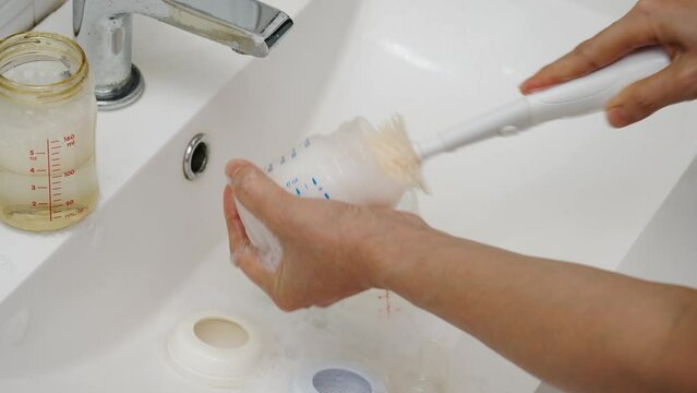 mother hand washing the baby plastic milk bottle