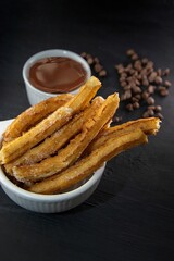 A vertical shot of churros next to a bowl of chocolate