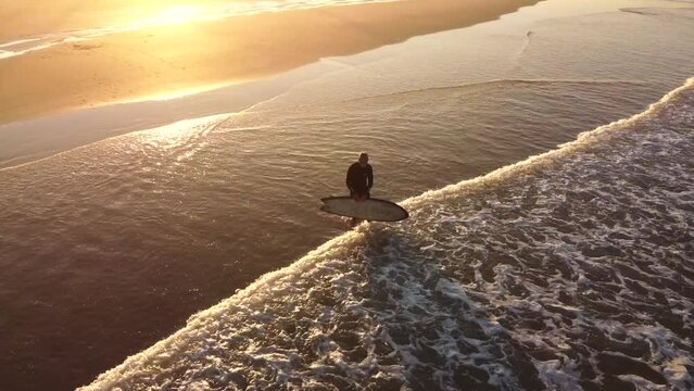 Aerial shot of a person with a surfboard entering the sea