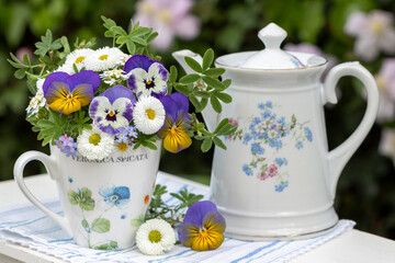 Arrangement mit Blumenstrauß mit lila Hornveilchen, Bellis in Tasse und vintage Kaffeekanne