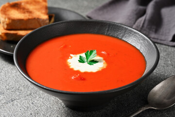 Close-up of a bowl of tomato soup on a gray stone background.