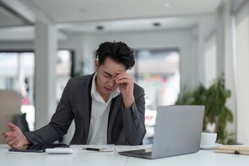 Tired exhausted business man office worker sitting at his desk tired of working in a laptop, overworked, having a headache, closed his eyes, needs rest and break