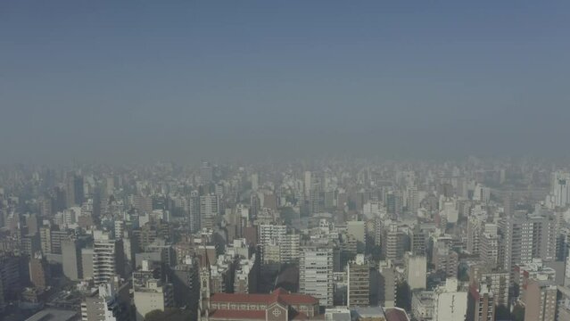 Aerial footage over the modern city of Rosario with buildings covered in smoke, air pollution