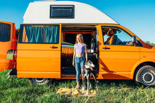 The happy girl with the dog has fun on a wonderful camping day. Van life concept.