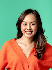 Fototapeta premium A studio portrait of a beautiful young Asian Indonesian woman wearing an orange shirt. Isolated on a green background.