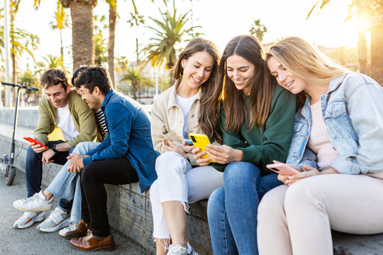 Teenage group of young friends using mobile phones outdoors. Millennials having fun watching social media content on smartphone app. Technology and youth community concept.