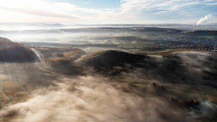 Aerial shot over a village and cultivated lands covered in fog at a sunny sunrise