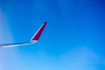 Closeup shot of an airplane wing in red and white colors isolated on the blue sky
