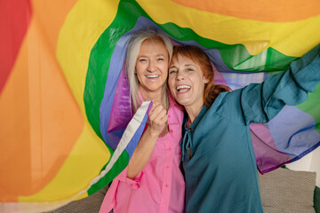 two senior mature women hoist the gay rainbow flag. I support the lgbti, gay, homosexual, bisexual, lesbian, trans, non-binary community. Fight for freedom and rights - obrazy, fototapety, plakaty