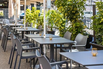 Outdoors cafe with gray chairs and tables on a sunny day with potted plants in the background