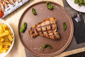 Top view of grilled T-bone steak with chilis served with brown plate in restaurant