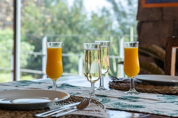 Horizontal shot of four glasses of orange juice and champagne on a wooden table with tableware on it