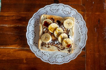 Horizontal shot of a toast with freshly cut bananas and chocolate on a white plate on a wooden table