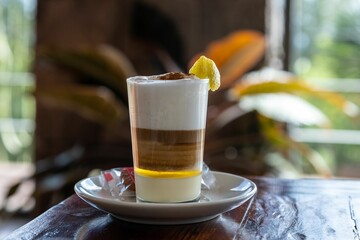 Horizontal selective focus of a barraquito shot on a brown wooden table with a lemon peel in it