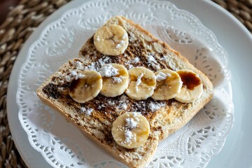 Horizontal closeup of freshly cut bananas, chocolate and sugar powder on toast on a white plate