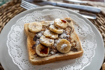 Obraz na płótnie Canvas Horizontal closeup of freshly cut bananas, chocolate and sugar powder on toast on a wooden table