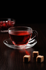 Glass cup with hot tea and brown sugar cubes on a black background. Selective focus.