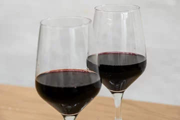 Fotobehang Closeup shot of two glasses of red wine on a wooden surface © Damián Méndez/Wirestock Creators