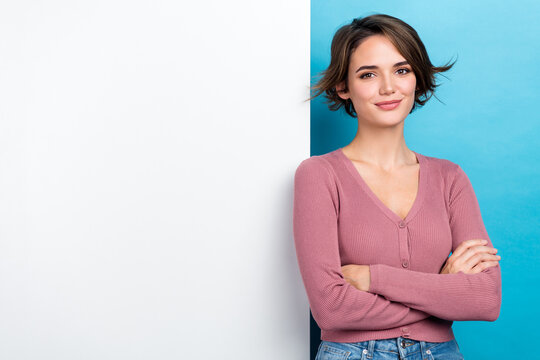 Portrait of good mood nice girl wear pink cardigan arms crossed stand near white board empty space isolated on blue color background