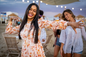 Beautiful party girl dancing and waving hands on the beach, young female friends on background