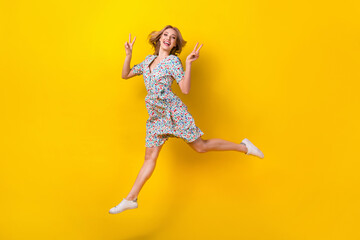 Fototapeta na wymiar Full length photo of cheerful excited lady wear flower print dress jumping high showing v-signs isolated yellow color background