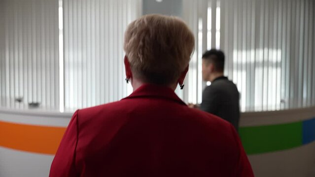 The teacher goes to the counter to register for a business meeting. Red clothes.