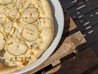 pear and cheese pizza on a white plate in a street cafe stands on a wooden table