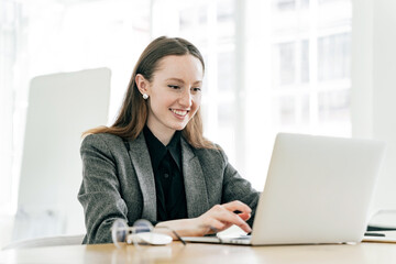 A freelancer student is a young woman working in an office, online learning education remotely, using a laptop in the workplace.