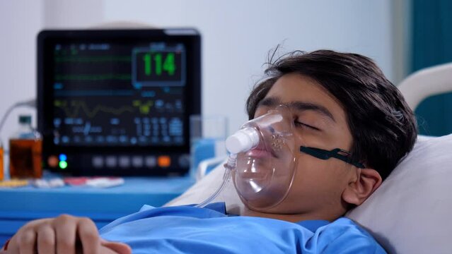 A sick boy is recovering in the hospital ward - health and medical  medical treatment. Close shot of hospital monitor / patient monitor displaying vital stats of a young male patient - oxygen mask ...
