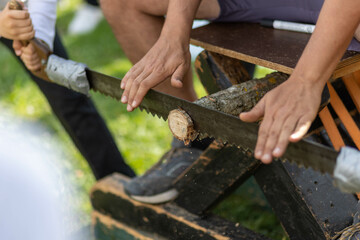 Un homme est assis sur un rondin de bois, et des personnes coupe le bois avec une scie