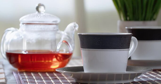 Pouring black tea into a ceramic cup on a wooden table. Tea break time. Pouring tea into cup of tea. Teapot pouring in cup 