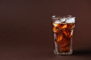 A glass of cola drink with ice cubes. Fresh cold sweet cola drink with ice one brown background with copy space.
