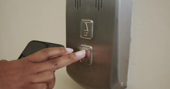 Hand of african american woman holding smartphone and calling elevator in office, in slow motion