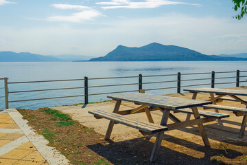 Empty wooden picnic tables and benches by the seafront on a bright summer day in Greece.