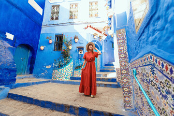 Young woman with red dress visiting the blue city Chefchaouen, Marocco - Happy tourist walking in Moroccan city street - Travel and vacation lifestyle concept - obrazy, fototapety, plakaty