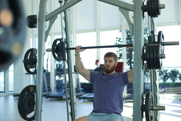 Young athletic man is training in the gym doing exercise with barbell