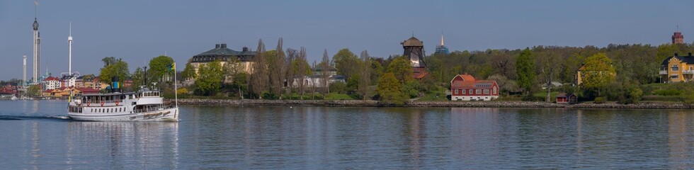 Obraz premium A modern commuting ferry leaving for the archipelago passing the cliffs of the district Södermalm part Sofo, a tranquil sunny summer day in Stockholm