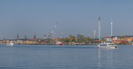 Fototapeta premium Commuter boats leaving piers for the archipelago, the old town Gamla Stan, the wharf island Beckholmen, towers, Tivoli in the background, a tranquil sunny summer day in Stockholm