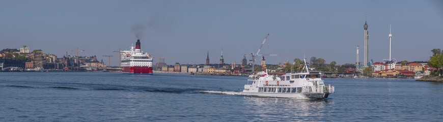 Fototapeta premium A cruise RORO ferry arriving at the ferry terminal, an inner archipelago commuting ferry passing on the way from down town piers, a tranquil sunny summer day in Stockholm