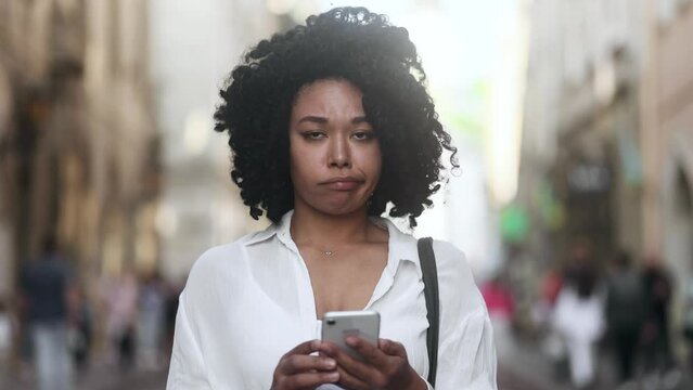 Pretty young curly african american woman thinks questioningly finding solution and show smartphone with green screen chroma key advertising template for your design at city screen Like Recommendation